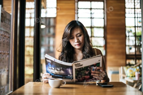 Preview: Beautiful woman reading magazine in cafe