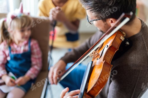 Preview: Happy single father smiling at his daughter while playing a violin at home.