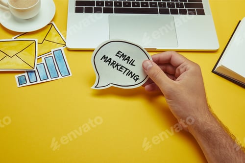 Preview: cropped image of man holding speech bubble with"email marketing" lettering near laptop