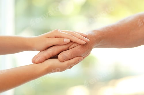 Preview: Young woman holding elderly man hand on blurred background, closeup. Help service