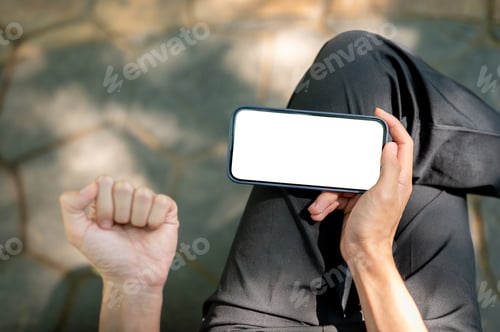 Preview: Top view a hand holding white screen smartphone horizontally and making a fist while sitting in park