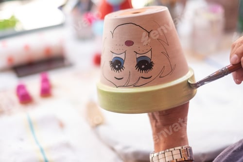 Preview: Art, creativity and people concept - close up of female artist painting a flower pot in studio
