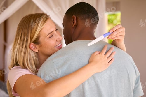 Preview: Hugging Multi-Racial Couple In Bedroom At Home Celebrating Positive Pregnancy Test Result