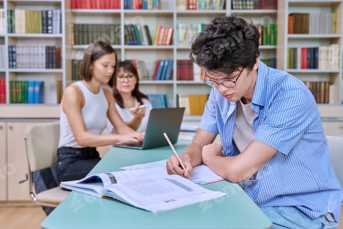 Preview: Portrait of student guy at desk inside college library, female student together with teacher