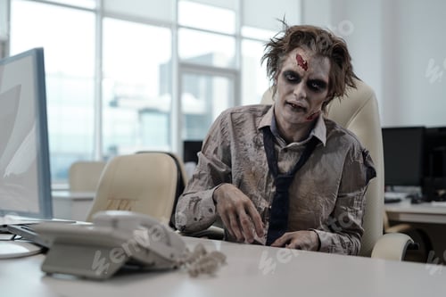Preview: Zombie businessman sitting by desk in office