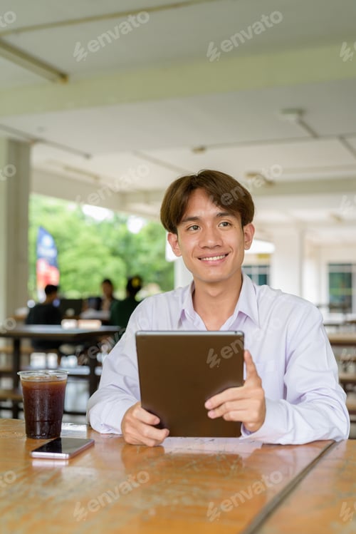 Preview: Non binary university student sitting in college campus using tablet computer