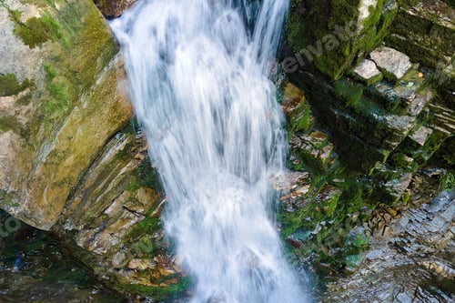 Preview: Waterfall on mountain river with white foamy water falling down from rocky formation in summer