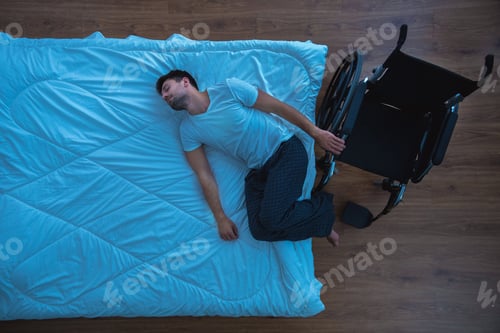 Preview: The man laying on the bed near a wheelchair. view from above, evening night time