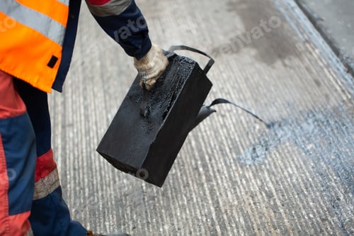 Preview: A worker pours liquid asphalt, molten bitumen from a bucket of resin.