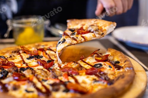 Preview: Hand of man holding slice of pizza over table against restaurant background