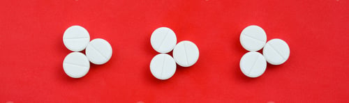 Preview: Several white tablets lie on a bright red background in the form of three triangular arrows