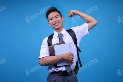 Preview: Portrait Of Indonesian High School Student Man Showing Strong Gesture On Blue Background