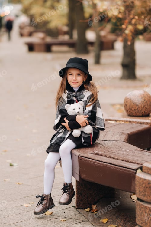 Preview: A little stylish girl in autumn clothes is sitting on a bench in the autumn city