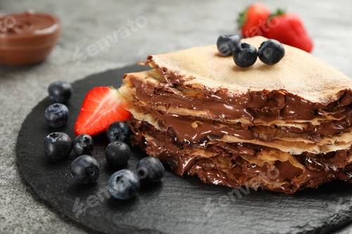 Preview: Delicious thin pancakes with chocolate paste and berries on slate plate, closeup