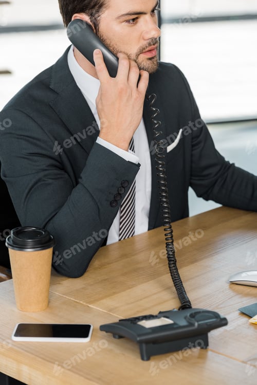 Preview: handsome businessman talking by stationary telephone in office