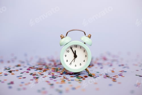 Preview: Alarm clock showing five minutes to twelve on a purple background with milticolored sequins.