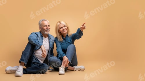 Preview: Smiling Senior Couple Sitting on Floor Pointing Upward