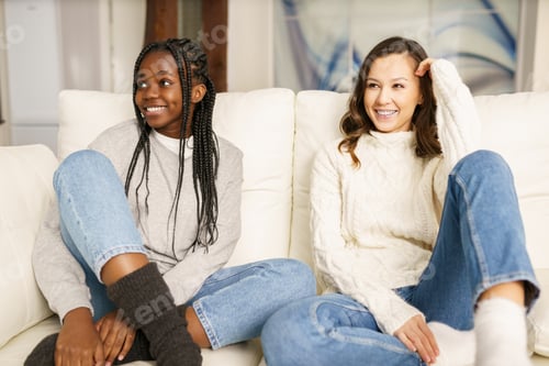 Preview: Two female student friends smiling together on the couch at home