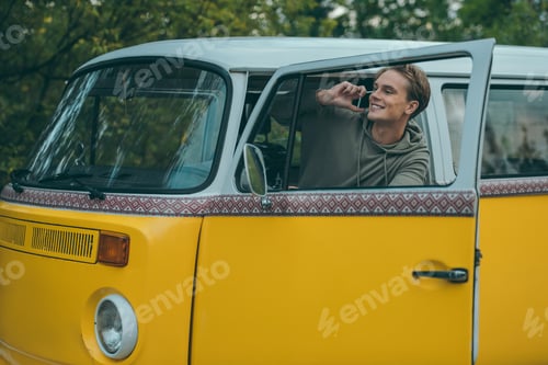 Preview: handsome young man using smartphone while sitting in retro minivan