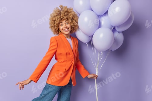 Preview: Horizontal shot of curly haired young woman dressed in stylish formal jacket and jeans holds bunch