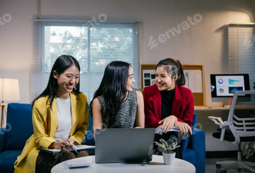 Preview: Three young businesswomen are smiling and collaborating on a project, using a laptop and documents i