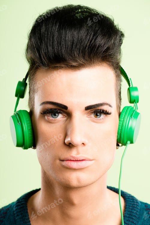 Preview: Shot of a handsome young man standing alone in the studio and listening to music through headphones