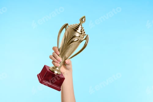 Preview: Woman holding gold trophy cup on light blue background, closeup