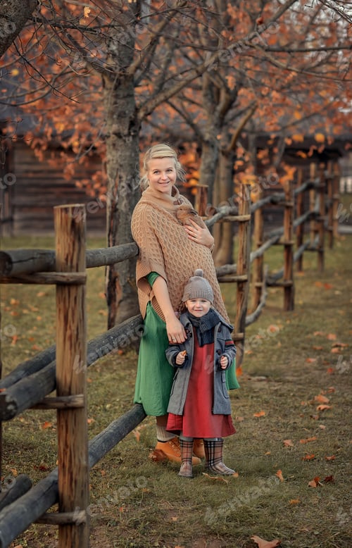 Preview: pregnant girl mom sits with her son near the house on the bridge in autumn in the village