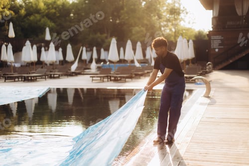 Preview: Pool maintenance worker removing cover at sunrise from hotel pool