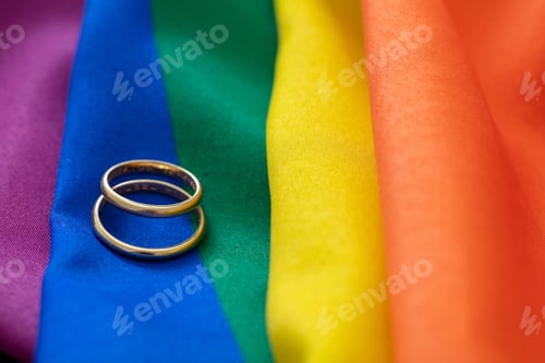 Preview: LGBT Gay marriage. Pair of golden rings on rainbow color textile, close up view. Copy space