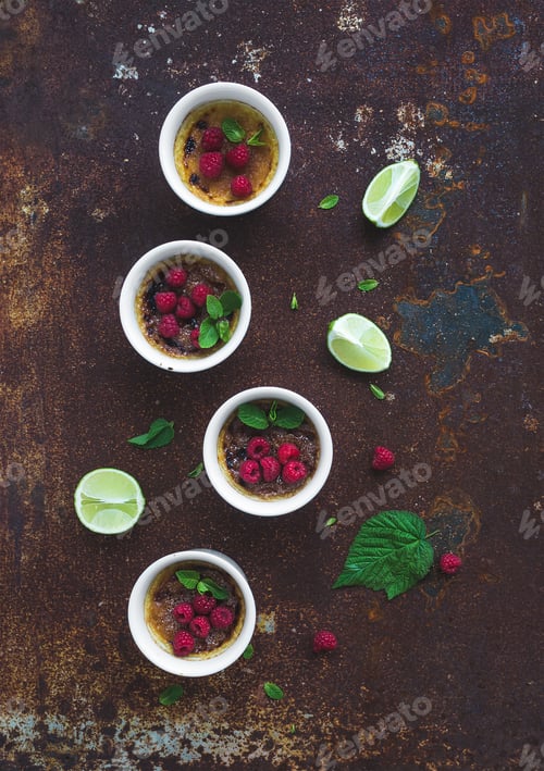 Preview: Creme brulees with raspberries and mint in white bowls over grunge metal backdrop. Top view
