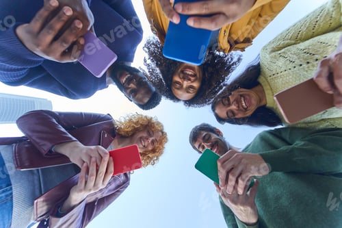 Preview: Happy young students using smartphones standing in circle outdoors