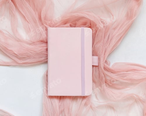 Preview: Pink hardcover notebook on tulle fabric on white table top view, textbook mockup