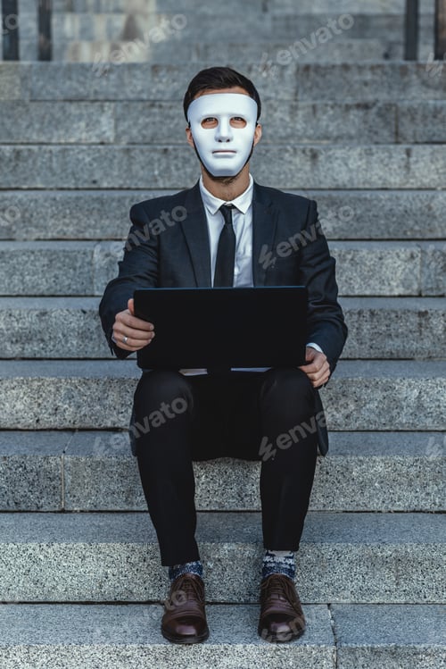 Visualização: Businessman with a face mask and a laptop looks straight. Sits on the steps of a business building