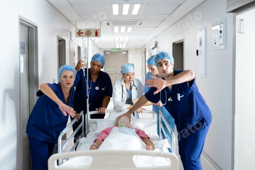 Preview: Diverse group of healthcare workers clearing the way for patient in bed in hospital corridor