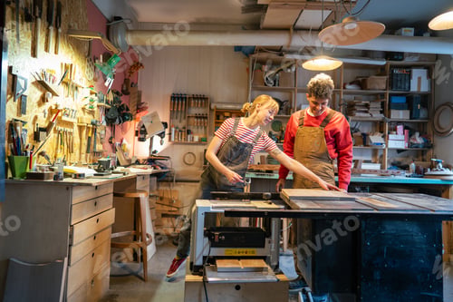 Preview: Enthusiastic couple of carpenters prepare stool base for saw machine in workshop. Apprentice teach