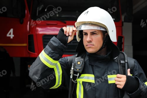 Preview: Portrait of firefighter in uniform and helmet near fire truck at station