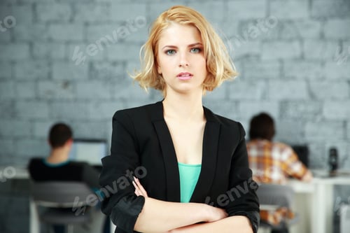 Preview: Portrait of a young pensive woman standing with arms folded in office