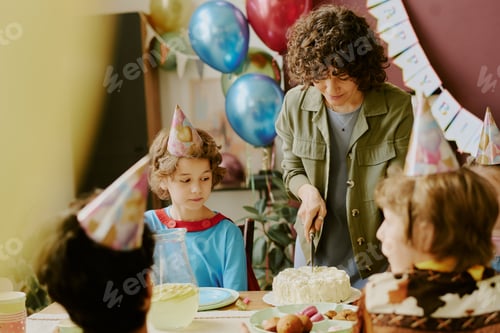 Preview: Caucasian Woman Cutting Birthday Cake for Group of Children at Party Table
