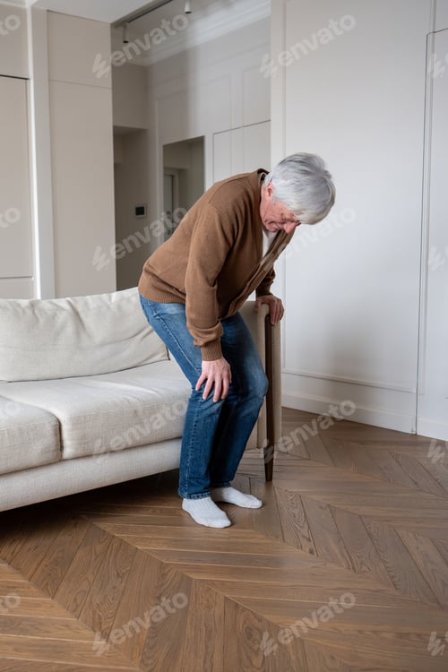 Preview: Old man suffering with knee joint pain. Elderly male howls struggling to rise from couch, arthrosis