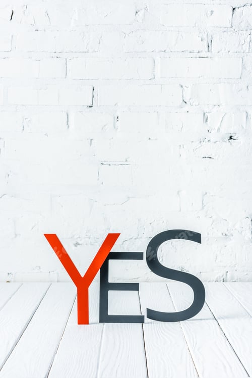 Preview: yes lettering with decorative red and black letters on wooden surface with white brick wall at