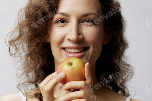 Preview: Closeup portrait of cheerful cute curly beautiful woman in basic white t-shirt enjoy apple smiling