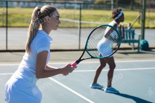 Preview: Caucasian female player playing game with african american doubles partner at tennis court