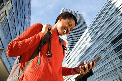Preview: Close up happy young black woman walking in city and looking at mobile phone