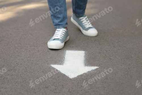 Preview: Person standing near arrow on asphalt, closeup