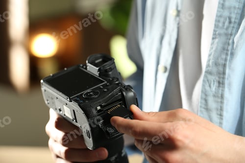 Preview: Man inserting SD memory card into photo camera indoors, closeup