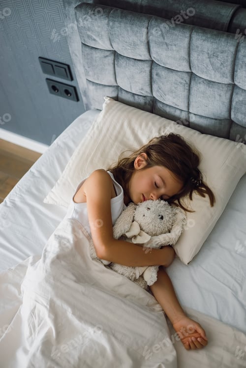 Preview: Sweet little girl peacefully sleeping and holding a toy bunny in her comfortable bed