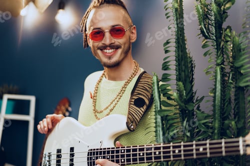 Preview: Young fashionable man in pink sunglasses playing guitar with joy