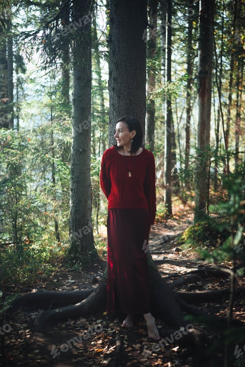 Preview: Woman stands beside tree in forest during daytime