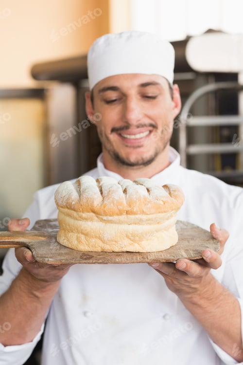 Preview: Baker showing freshly baked loaf in the kitchen of the bakery